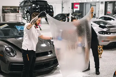 Detailers holding a sheet of paint protection film next to a sports car
